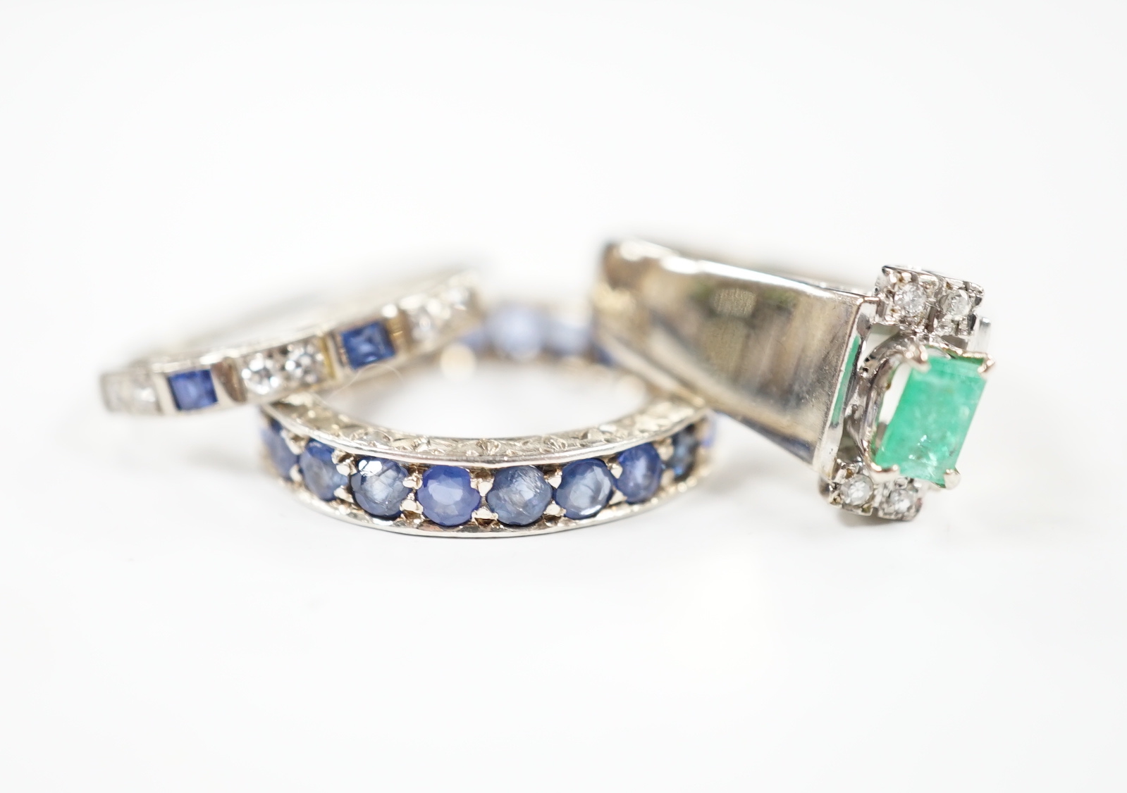 An 18k white metal, emerald and diamond set dress ring, size O, a white metal and sapphire set full eternity ring (stones missing) and an 18ct, sapphire and diamond set half hoop ring, gross weight 10 grams.